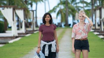 Something in the Water: Two young women stand together with palm trees and sun beds behind them