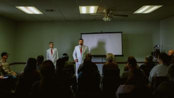 Sovereign Movie: White-suited Jerry Kane speaks to a crowd in a conference room, his nearby son, Joe, dressed alike