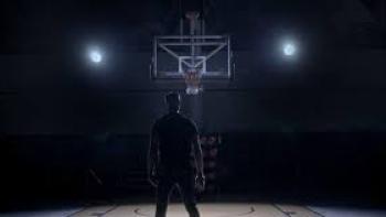 Stand: In darkened basketball court, the back of Black man standing center faces basketball hoop