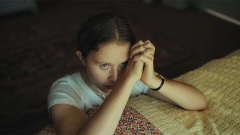 The Starling Girl Movie: A girl kneels next to a bed, her hands in a prayer position