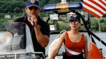 Striking Distance: Police officers on a boat, one uses a radio, with an American flag in the background.