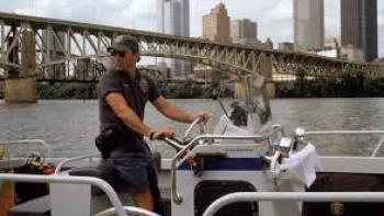Striking Distance: Bruce Willis steers a boat on a river with a city skyline and bridge in the background.