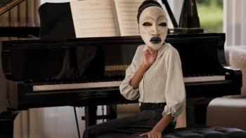 Strung: person in a white mask sitting by a piano in a well-lit room.
