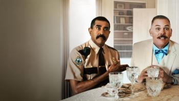 Super Troopers 3 Movie: Two men sit at a table, one in a Trooper uniform, the other in a beige suit