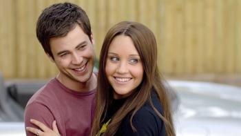 Amanda Bynes and Matt Long stand in an embrace, both smiling at something off-camera.