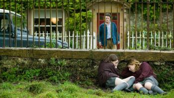 Tamara Drewe: Luke Evans comes out of the front door of a cottage, while two teenage girls duck behind a wall to remain unseen