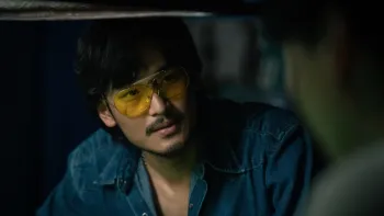 Tee Yai: Born to be Bad movie: Thai man in blue shirt and Aviator sunglasses center speaks to someone in a dark room 