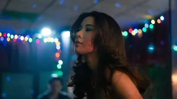 Tee Yai: Born to be Bad movie: Thai woman with long black hair center dances in a bar night club, colorful lights adorn stage behind her