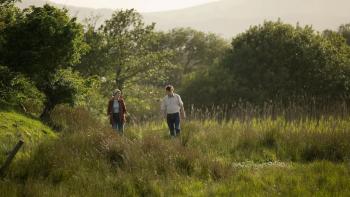 That They May Face the Rising Sun: A White man and woman walk through long grass together