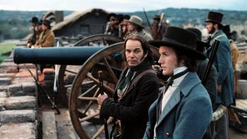 The Alamo movie: Two White men in 1830s clothing stand next to a cannon