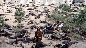 The Alamo movie: A battle-weary man kneels on the ground looking anguished, surrounded by dead bodies and encampments