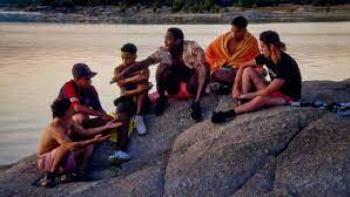 The Bad Family: Men sit on a rock by a lake