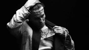 The Bride! Movie: The monster, with his hand on his scarred head, pulls his jacket open to expose a chest full of tattoos