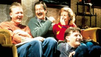 The Castle: A White family of four sit together on and near a couch laughing together 