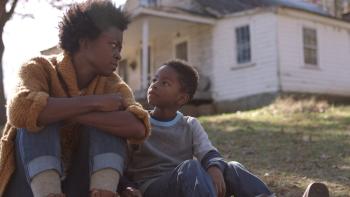 The Devil to Pay movie: a Black woman on left sits on the lawn outside a house with her Black son on right