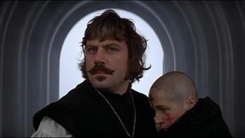 The Devils: Man with mustache holding a woman with a shaved head in a hallway