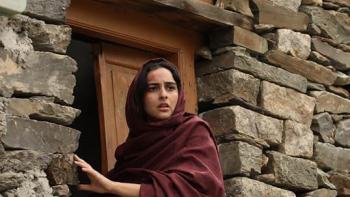 The Diplomat: Woman in a maroon shawl looks anxiously out from a stone doorway in a rural setting