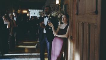 The Drama movie: Mamoudou Athie and Alana Haim lean against a wall in formal attire at a wedding, holding wine and looking judgmental