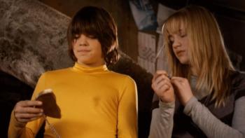 The Gold Retrievers movie: A boy in yellow mockneck and girl look down at a broken gold coin on a chain