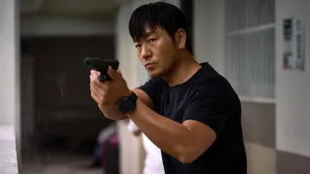 The Great Flood movie: Park Hae-soo in a black t-shirt points a gun forward while standing on an apartment balcony