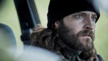 The Hanging Sun: Hitman John stares intensely out of a car window while wearing a beanie hat