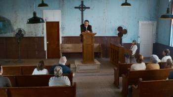 The Hill Movie: A White middle-aged man wearing a suit stands on the pulpit preaching to a half-full church congregation