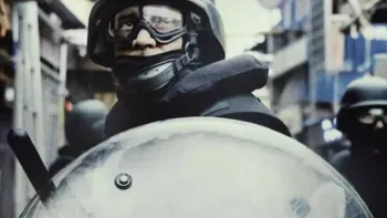 The Kitchen: A close-up of a policeman in riot gear, complete with shield and truncheon.
