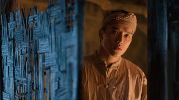 The Last Wife movie: Vietnamese man in tan shirt and headband stands in doorway on right