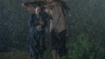 The Last Wife movie: Vietnamese man and woman center run in the rain under a straw mat