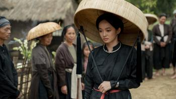 The Last Wife movie: Vietnamese woman in large straw hat and black gown walks in village while villagers look on
