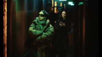 The Moment movie: Charli XCX walks through a hallway with her sunglasses and a thick coat on, her female assistant texting behind her