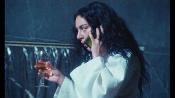 The Moment movie: Charli XCX wears a bathrobe, drinking wine and talking on a phone held to her ear