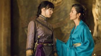 Michelle Yeoh and Isabella Leong stand chatting in a tomb-like hallway, wearing Chinese Hanfu.