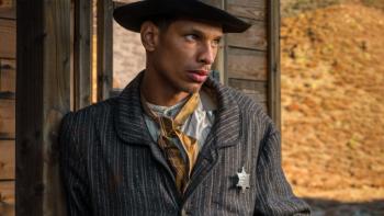 The Night They Came Home movie: Black man in sheriff's jacket in old west center leans against wooden house