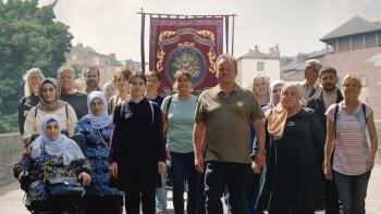 The Old Oak: A group of people, some English and some Syrian, stand together in front of an embroidered banner in the street