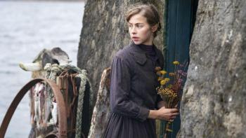 The Road Dance: A young woman stands looking over her shoulder, holing a bunch of flowers outside a cottage door