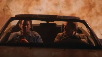 The Rookie (1990) movie: Charlie Sheen left, Clint Eastwood right, sit in the front of a convertible car with top gone, fire behind them