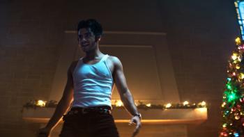 The Sacrifice Game movie: An Egyptian American man in white tank top center left stands menacingly next to Christmas tree on right