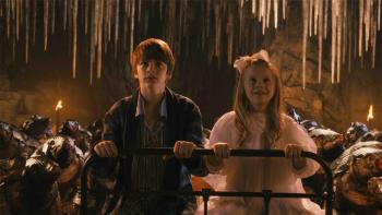 A brother and sister in their PJs sit atop their iron bed in an underground cavern