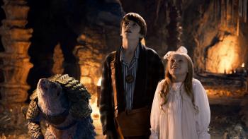 A brother and sister stand in an underground cavern next to a standing pangolin with a look of awe on their faces