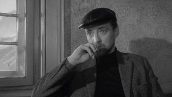 The Spy Who Came in from the Cold: A White man in a cap sits by a window while holding pen to his lips
