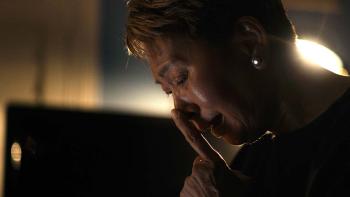 The Stringer: The Man Who Took the Photo movie: Vietnamese woman with short hair center holds hands to face while sitting in dark room