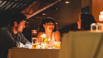 The Threesome movie: At a restaurant table, Josh Hauer-King looks at Zoey Deutch as she smiles across the table to Ruby Cruz
