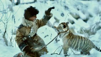 The Tiger's Nest: A young Indian boy lifts his hand to a baby tiger's paw in a high-five gesture, the two of them surrounded by snow.