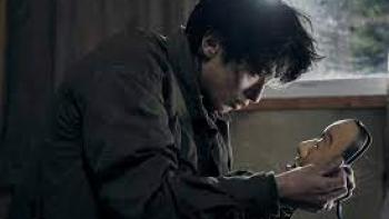 The Village (2023): A Japanese man center hunches over looking at a Japanese Noh mask in his hands
