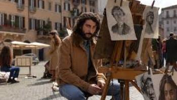 The Big Fake movie: Pietro Castellitto sits in a town square with paintings