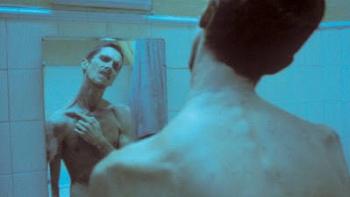 The Machinist Movie: Man with thin frame looking in a bathroom mirror with a blue tint.