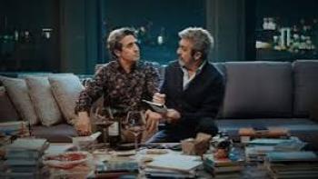 Therapy Done Right Movie: Two men sit on a couch, talking in a dimly lit room with books and snacks on the table.