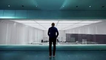 The Thinking Game Movie: Person standing in a blue-lit room, facing a large window into a modern white space.