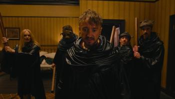 They Will Kill You Movie: Wearing a black cloak, Kevin (Tom Felton) is with four others, armed with sticks, looking shocked